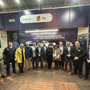 Foto horizontal colorida mostra grupo grande de pessoas posando para a foto dentro do estande da feira