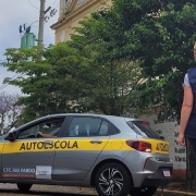 Foto horizontal colorida mostra um exame prático de direção. Carro de autoscola realiza manobra da baliza enquanto a examinadora de colete do DetranRS observa