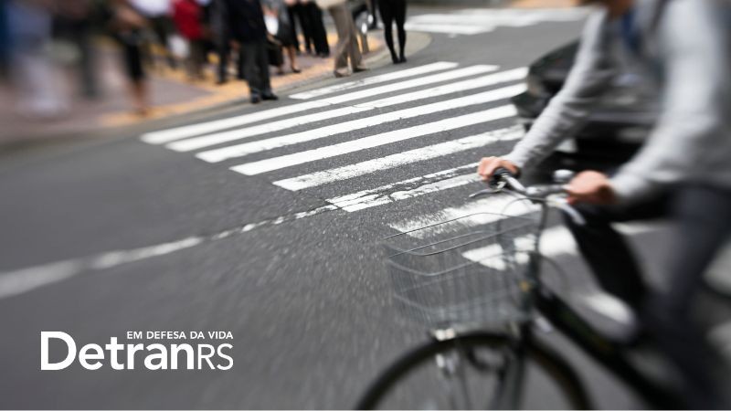 parte de uma bicicleta e ciclista em primeiro plano passando por uma faixa de segurança de pedestres aguardando do outro lado na calçada