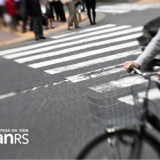 parte de uma bicicleta e ciclista em primeiro plano passando por uma faixa de segurança de pedestres aguardando do outro lado na calçada