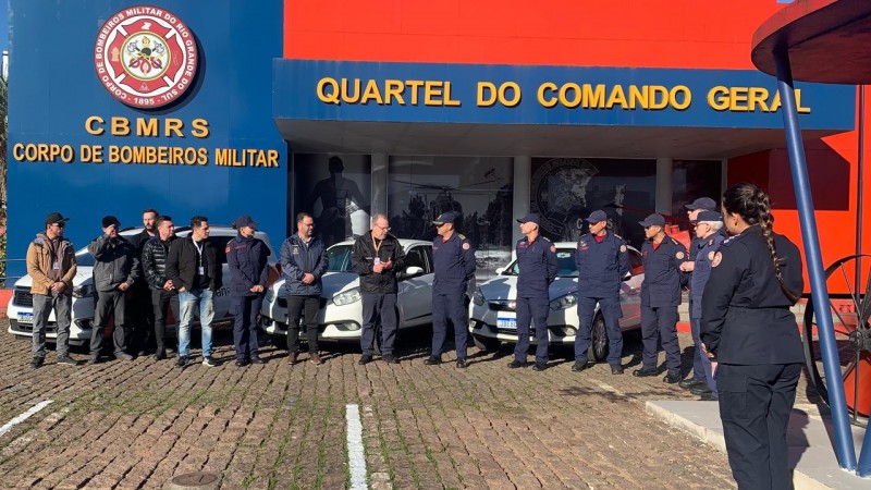 Foto horizontal colorida em frente ao Quartel do Comando-Geral mostra grupo de pessoas, metade delas uniformizada, em frente aos carros doados.