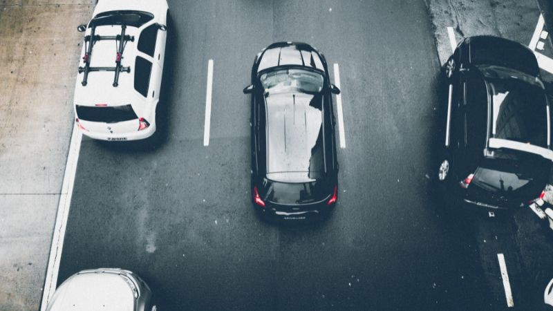 Foto horizontal colorida mostra carros em uma faixa de três pistas vistos de cima