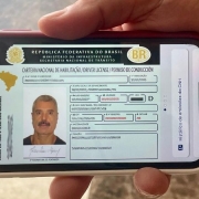 Foto horizontal colorida mostra mão segunrando um celular. Na tela, a CNH Social de um homem de bigode