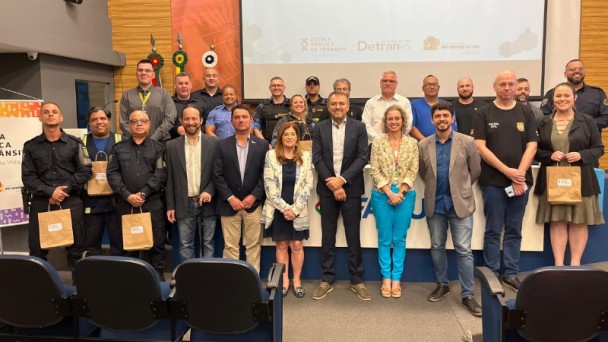 Foto horizontal colorida mostra grupo de formandos posando para a foto em um ambiente de auditório