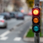 Foto horizontal colorida mostra semáforo no vermelho com ambiente de trânsito desfocado ao fundo