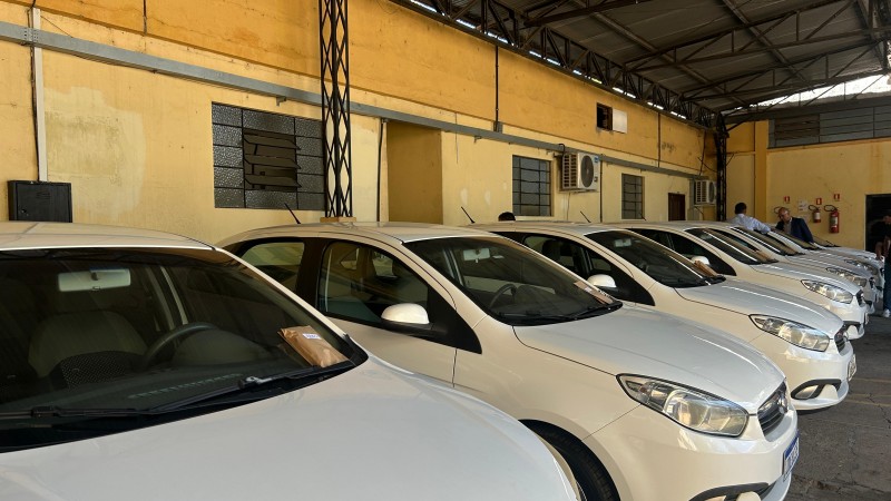 Foto horizontal colorida mostra fileira de carros brancos estacionados em um galpão